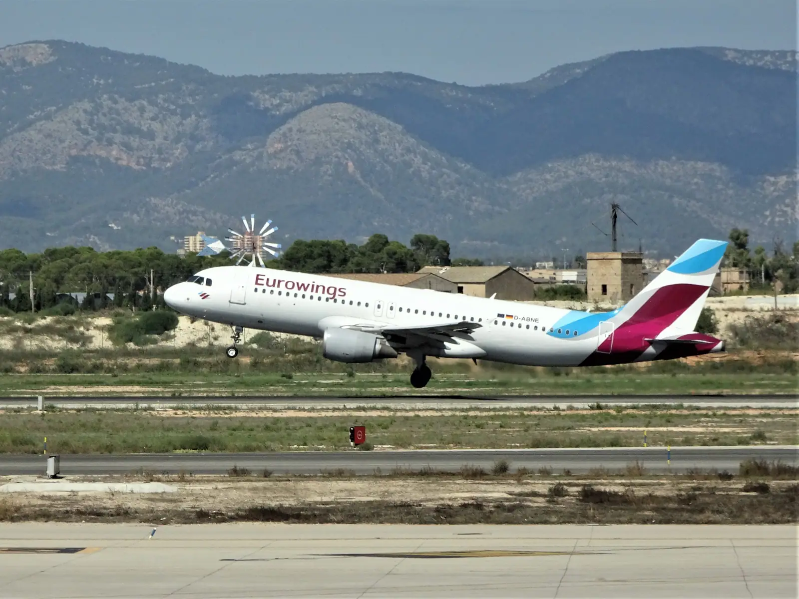 Un avion décolle de l’aéroport de Palma, devant un moulin à vent et les montagnes de Majorque