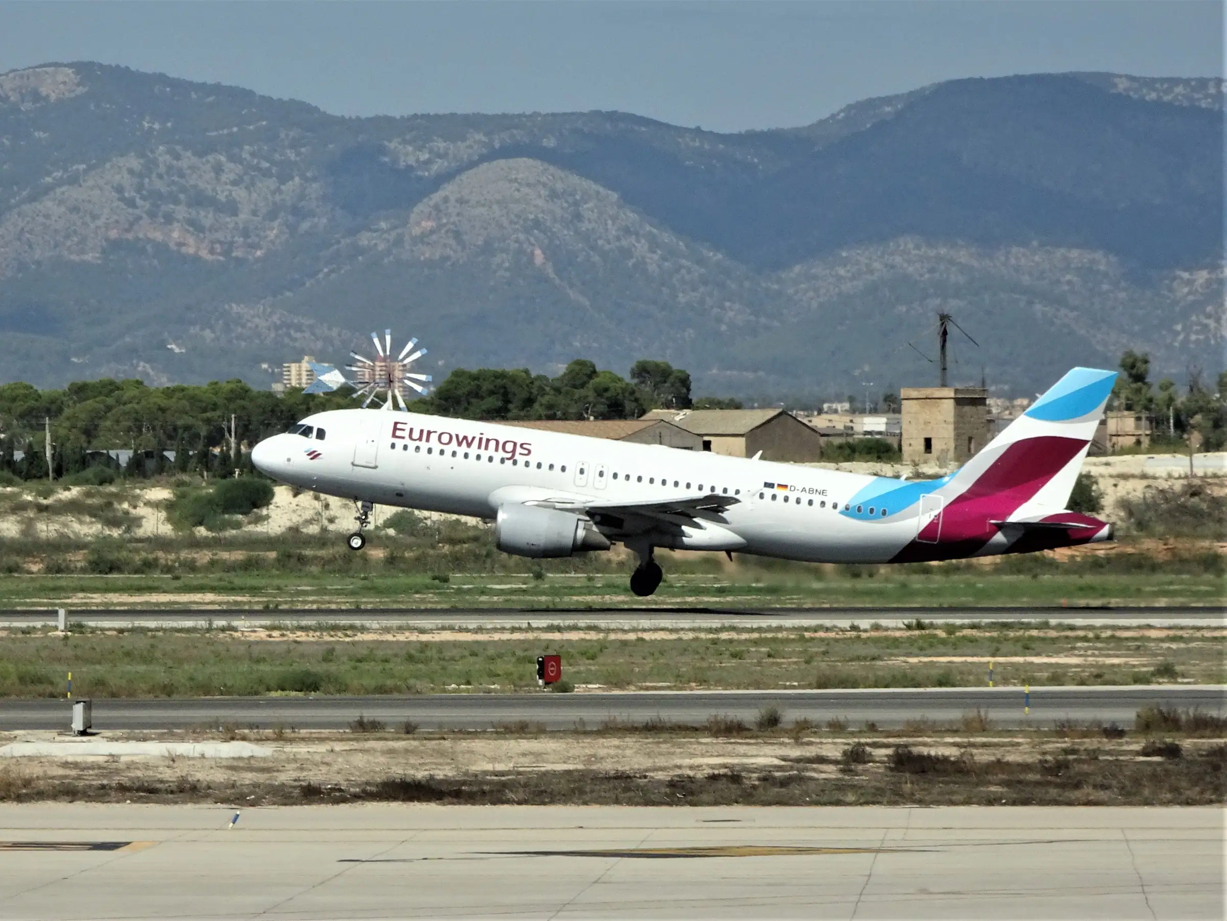 Un avion décolle de l’aéroport de Palma, devant un moulin à vent et les montagnes de Majorque