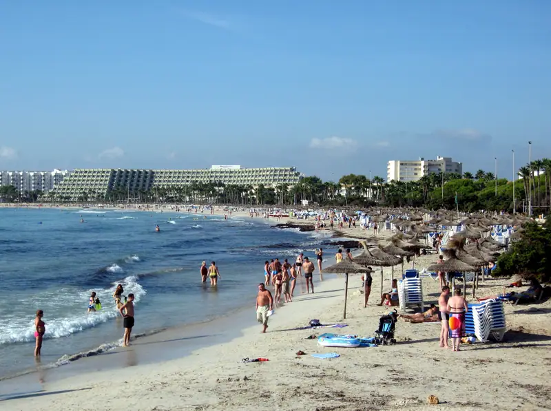 La plage de Sa Coma, parasols de paille et baigneurs sous un ciel bleu