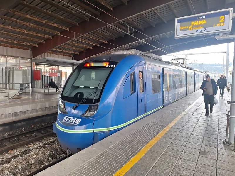 Un train SFM bleu en gare d'Inca, voyageurs sur le quai