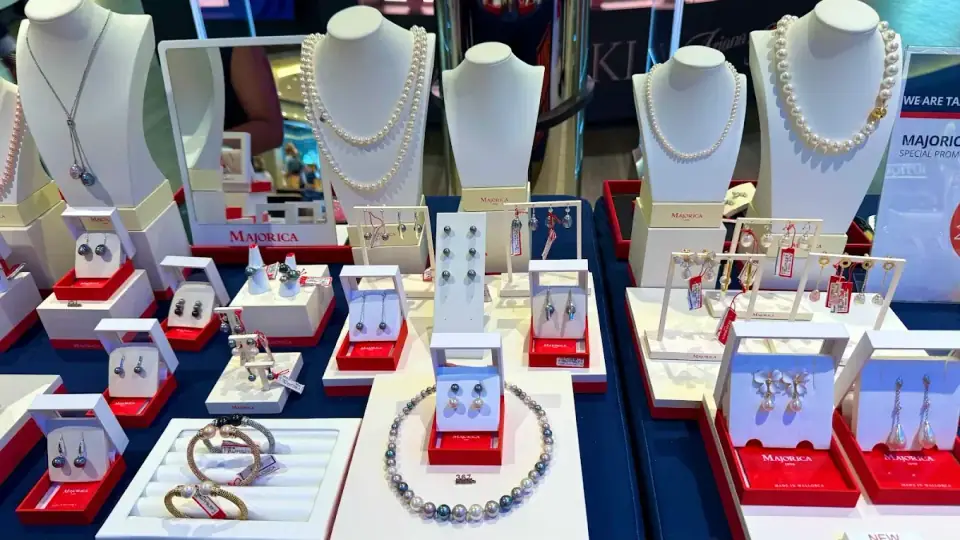 Présentoir de bijoux en perles de la marque Majorica, incluant des colliers, boucles d'oreilles et bracelets sur des supports blancs et dans des boîtes rouges.
