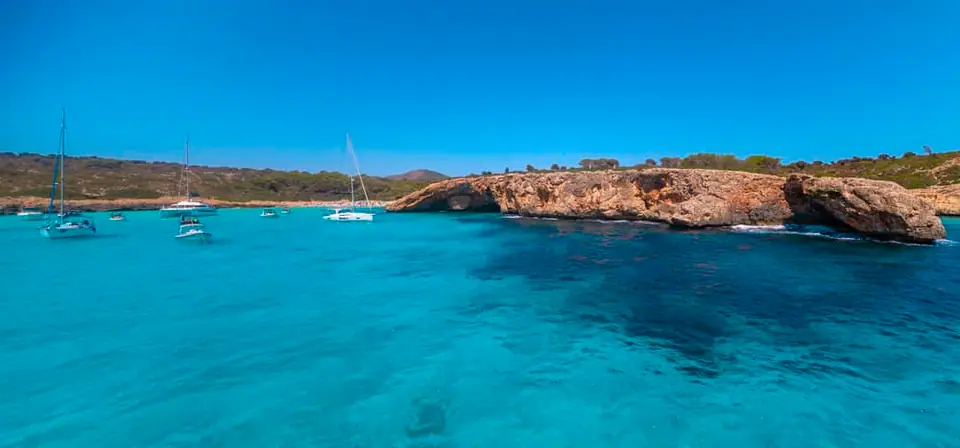 Crique sauvage de Cala Varques à Majorque avec son eau turquoise, ses bateaux au mouillage et son arche rocheuse naturelle.