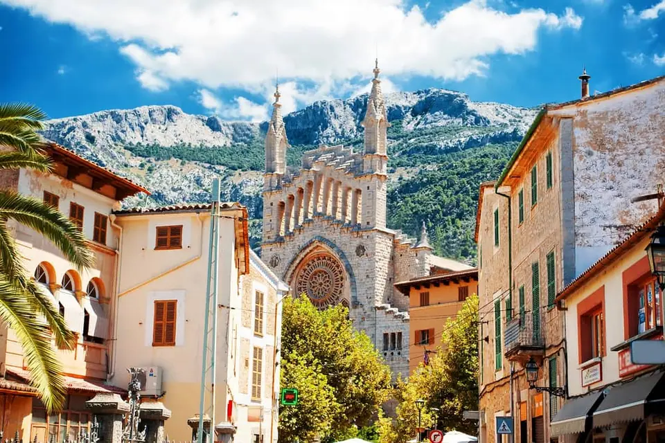 Façade moderniste en pierre grise de l'église Sant Bartomeu au centre du village de Sóller, adossée aux montagnes de la Serra de Tramuntana.