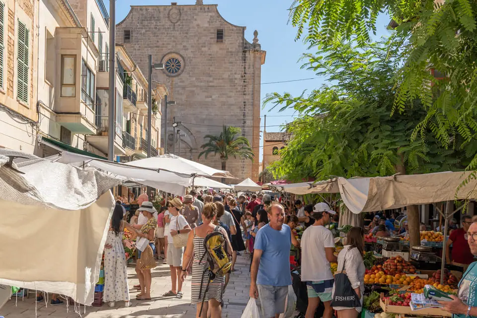 Foule et étals de fruits frais dans les rues pavées du marché de Santanyí, avec l'église en arrière-plan.