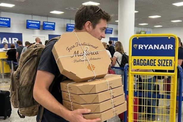Un passager tient une immense pile de boîtes d'ensaïmadas artisanales devant le comptoir d'enregistrement et le gabarit bagage à main Ryanair à l'aéroport de Palma.