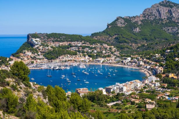 Vue panoramique en hauteur sur la baie en forme de fer à cheval du Port de Sóller à Majorque, montrant les bateaux amarrés et les montagnes de la Serra de Tramuntana en arrière-plan.