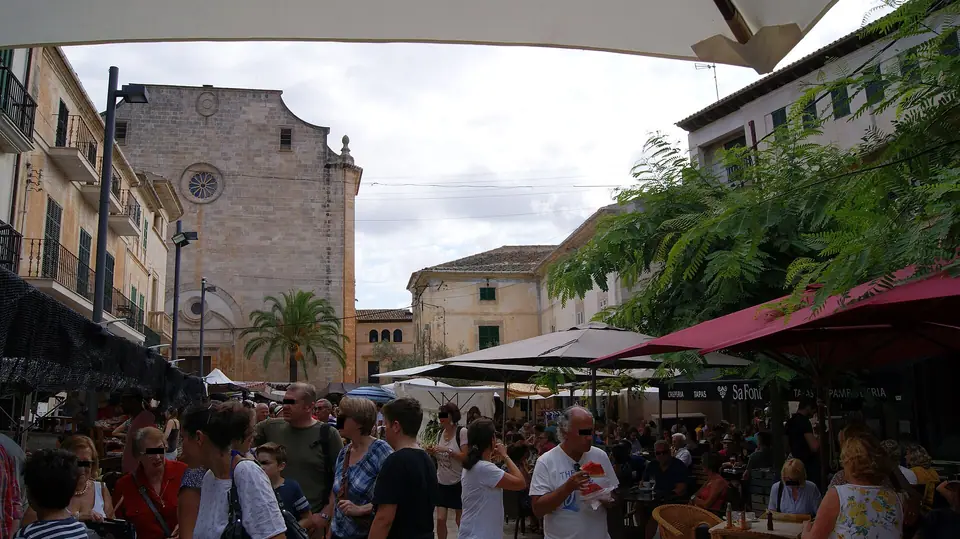 Photo : Asurnipal, CC BY-SA 4.0, via Wikimedia Commons Foule et étals sur la Plaça Major de Santanyí, devant l'église